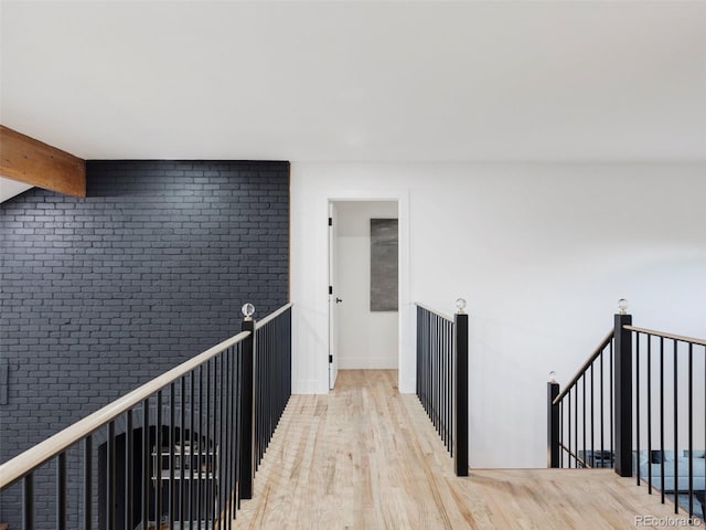 corridor with brick wall, an upstairs landing, baseboards, light wood finished floors, and beamed ceiling