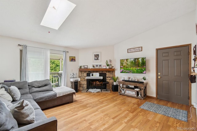 living room with wood-type flooring, a stone fireplace, and vaulted ceiling with skylight