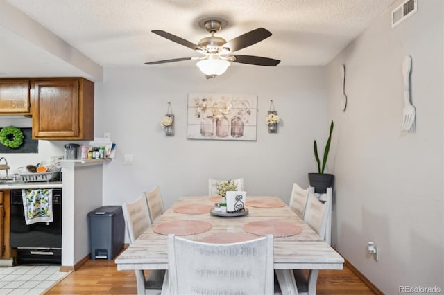 dining room with light wood-type flooring, ceiling fan, and a textured ceiling