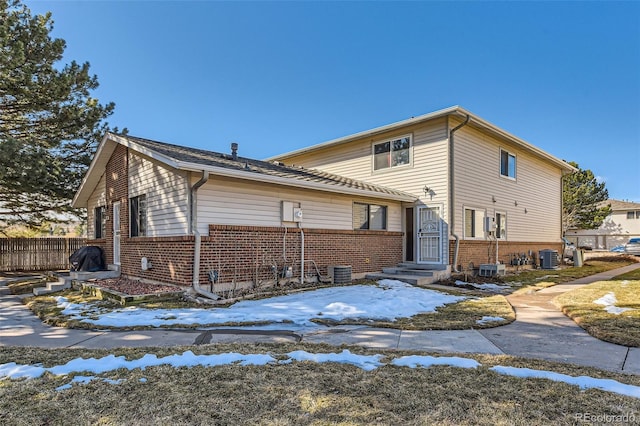 exterior space with central air condition unit, fence, and brick siding