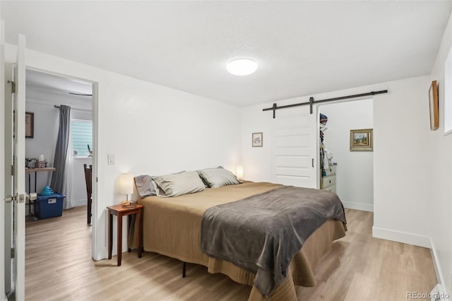 bedroom featuring a textured ceiling, a barn door, and light hardwood / wood-style flooring