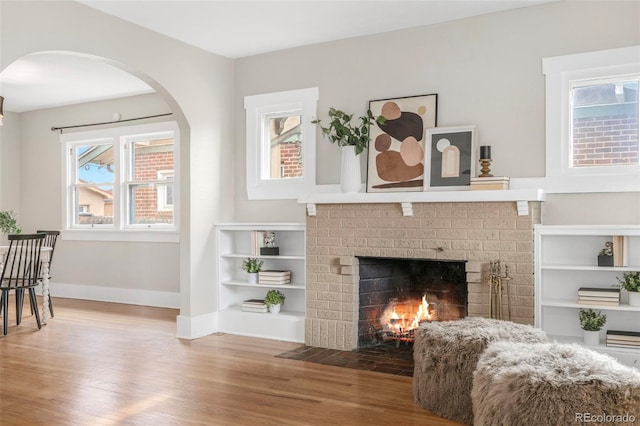 living area featuring a brick fireplace, baseboards, and wood finished floors