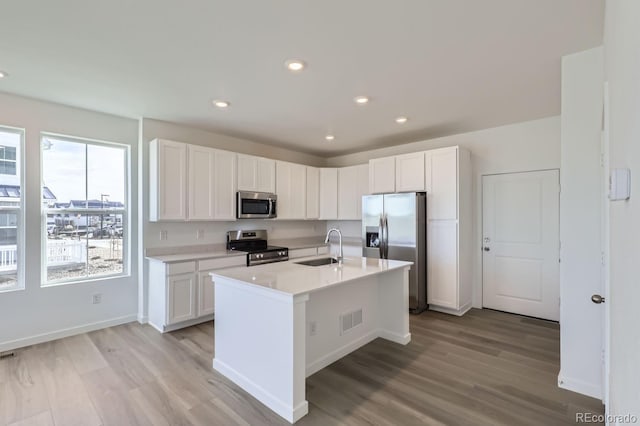 kitchen with light wood-type flooring, stainless steel appliances, sink, a center island with sink, and white cabinetry