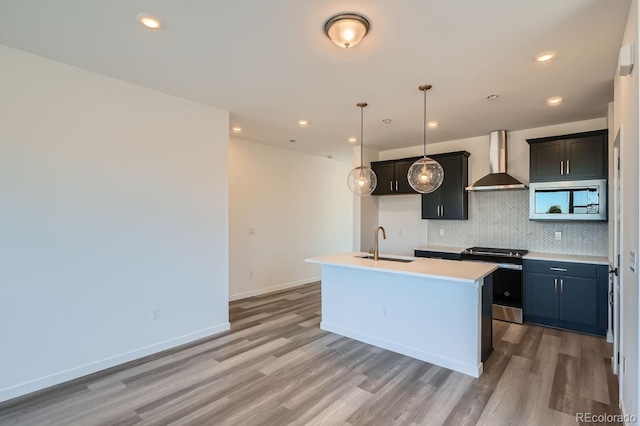 kitchen with sink, wall chimney range hood, wood-type flooring, a center island with sink, and appliances with stainless steel finishes