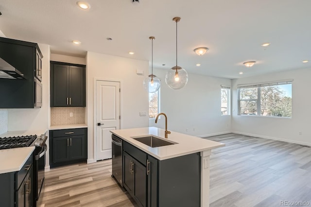 kitchen featuring appliances with stainless steel finishes, sink, pendant lighting, a center island with sink, and light hardwood / wood-style flooring