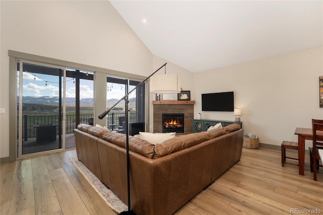living room featuring high vaulted ceiling, a tiled fireplace, light wood-style flooring, and baseboards