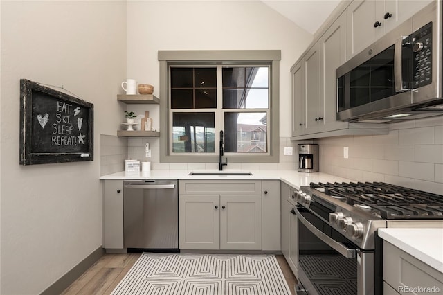 kitchen featuring appliances with stainless steel finishes, a sink, tasteful backsplash, light countertops, and light wood finished floors