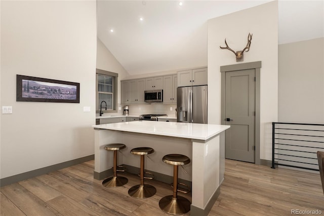 kitchen featuring appliances with stainless steel finishes, light wood finished floors, light countertops, a sink, and a breakfast bar