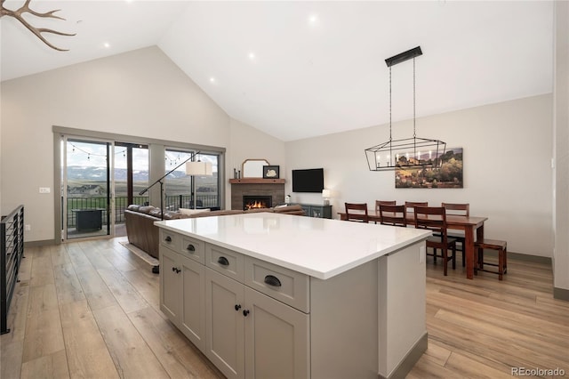kitchen with high vaulted ceiling, a lit fireplace, a center island, light countertops, and open floor plan