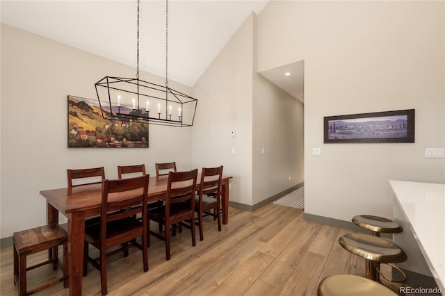 dining space with light wood-style flooring, high vaulted ceiling, baseboards, and a chandelier