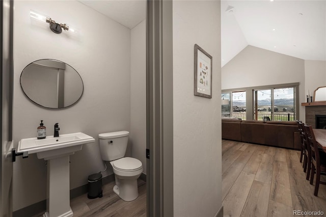 bathroom featuring lofted ceiling, wood finished floors, toilet, a fireplace, and baseboards