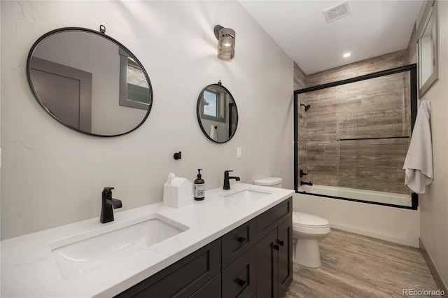 full bath with toilet, wood finished floors, double vanity, combined bath / shower with glass door, and recessed lighting