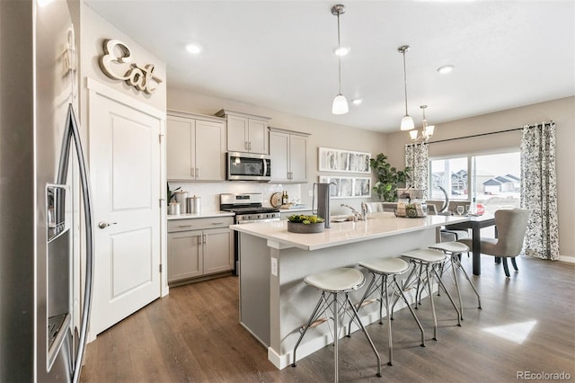 kitchen with gray cabinets, a breakfast bar, pendant lighting, an island with sink, and stainless steel appliances