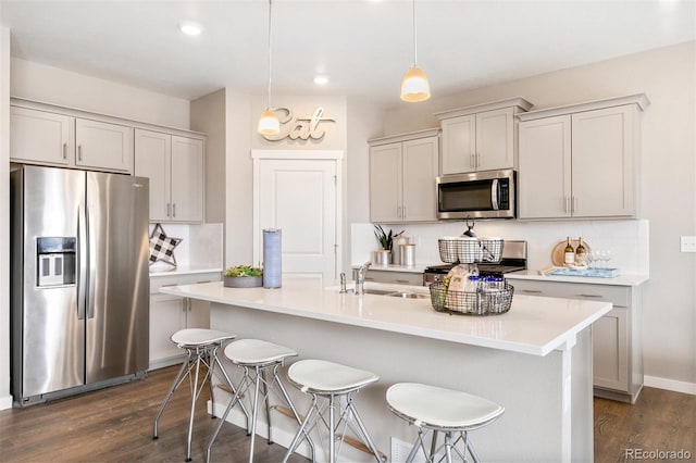 kitchen featuring a kitchen bar, sink, hanging light fixtures, appliances with stainless steel finishes, and decorative backsplash