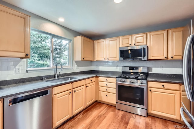 1616 Cedarwood Dr, Longmont, CO 80504 - kitchen with stainless steel appliances, dark countertops, light brown cabinets, light wood-style floors, and decorative backsplash