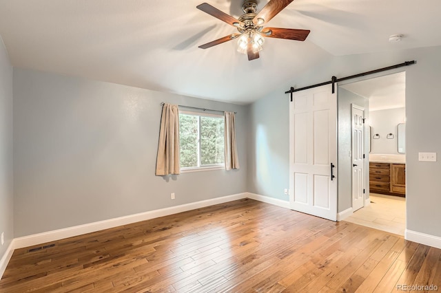 1616 Cedarwood Dr, Longmont, CO 80504 - unfurnished bedroom with a barn door, light wood-style floors, lofted ceiling, ensuite bathroom, and ceiling fan