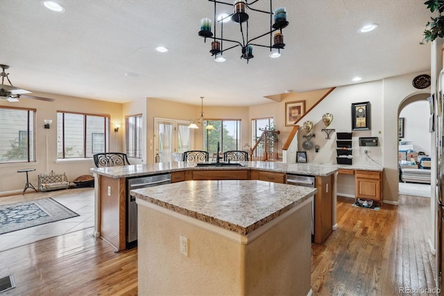 kitchen featuring ceiling fan with notable chandelier, dishwasher, a kitchen island, hardwood / wood-style floors, and decorative light fixtures