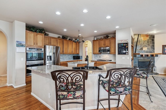 kitchen with stainless steel appliances, a stone fireplace, a breakfast bar area, a center island with sink, and light hardwood / wood-style floors