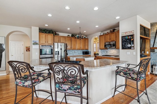 kitchen featuring decorative backsplash, a kitchen island with sink, light wood-type flooring, and stainless steel appliances