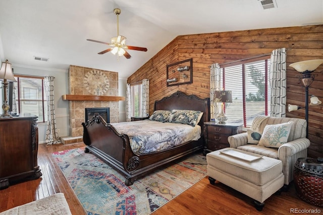 bedroom with ceiling fan, vaulted ceiling, a stone fireplace, and hardwood / wood-style flooring