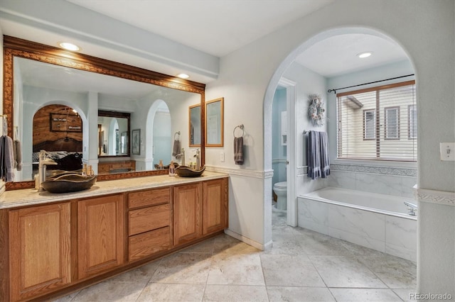 bathroom with tiled tub, toilet, tile patterned floors, and vanity