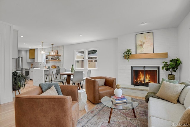 living room with recessed lighting, a brick fireplace, and light wood finished floors