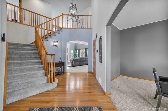 foyer with arched walkways, a notable chandelier, a towering ceiling, wood finished floors, and baseboards