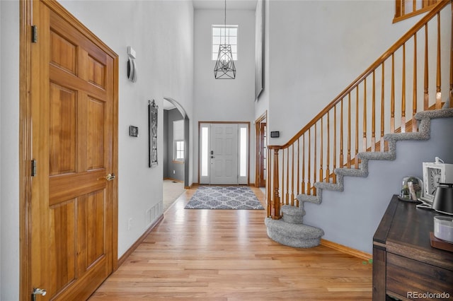 entryway featuring light wood-style floors, arched walkways, baseboards, and stairs