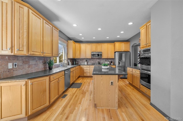 kitchen with a center island, light wood finished floors, stainless steel appliances, dark countertops, and decorative backsplash