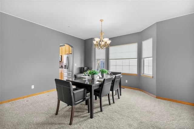 dining space with a chandelier, arched walkways, light carpet, and baseboards