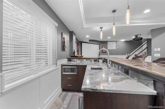 kitchen featuring light stone counters, stainless steel microwave, hanging light fixtures, dark brown cabinets, and a sink