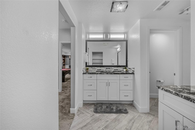 bathroom with visible vents, a textured ceiling, vanity, and baseboards