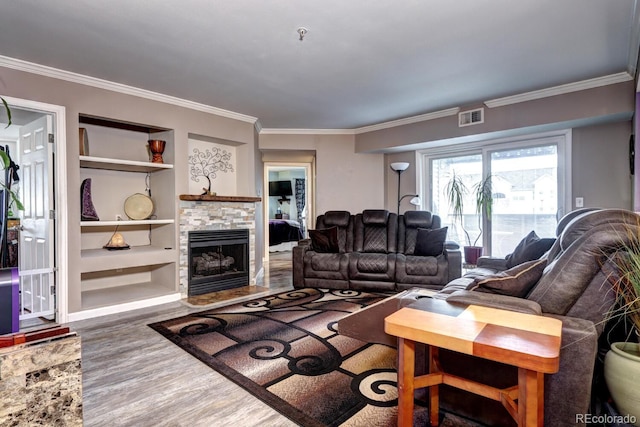 living room featuring a stone fireplace, visible vents, crown molding, built in shelves, and wood finished floors