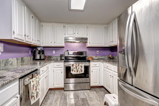 kitchen with under cabinet range hood, stainless steel appliances, white cabinets, and light wood-style floors