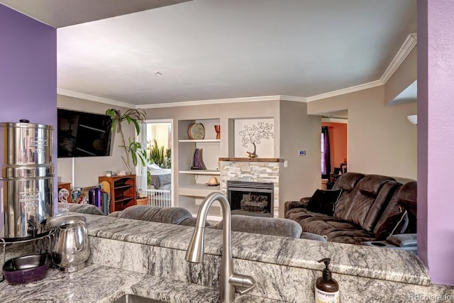 living room with crown molding, a stone fireplace, and built in features