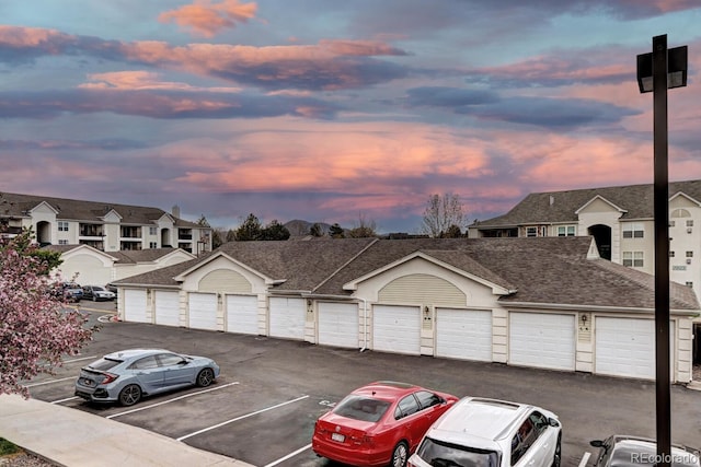 view of front facade featuring a shingled roof, a residential view, and community garages