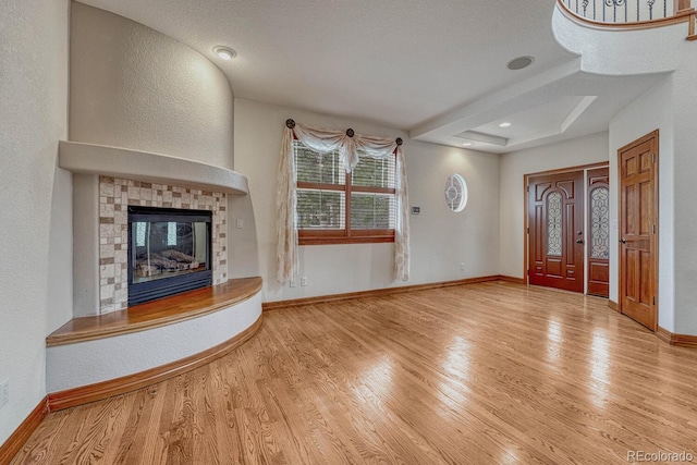 unfurnished living room with a glass covered fireplace, baseboards, a tray ceiling, and wood finished floors
