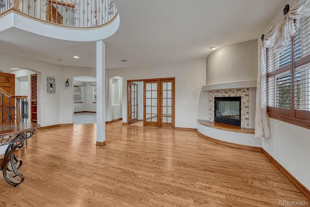 unfurnished living room with french doors, arched walkways, wood finished floors, a tile fireplace, and baseboards