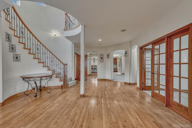 foyer with baseboards, arched walkways, stairs, and wood finished floors