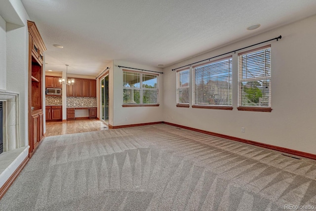 unfurnished living room with baseboards, light carpet, a textured ceiling, and a notable chandelier