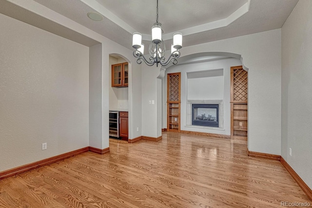 unfurnished living room featuring an inviting chandelier, arched walkways, light wood finished floors, and wine cooler