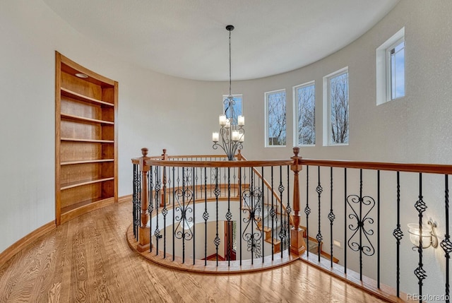 hall featuring built in features, wood finished floors, baseboards, a chandelier, and an upstairs landing