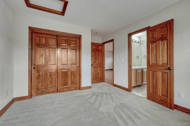 unfurnished bedroom with a closet, baseboards, light colored carpet, and ensuite bath