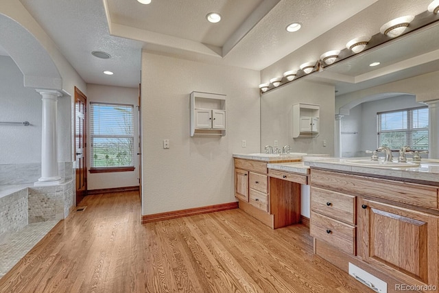 full bathroom featuring decorative columns, a wealth of natural light, a sink, and a raised ceiling
