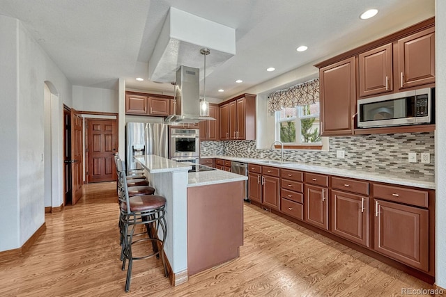 kitchen with a kitchen bar, island range hood, appliances with stainless steel finishes, a sink, and light wood-style flooring