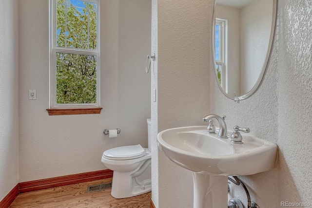 bathroom with toilet, a textured wall, a healthy amount of sunlight, and wood finished floors