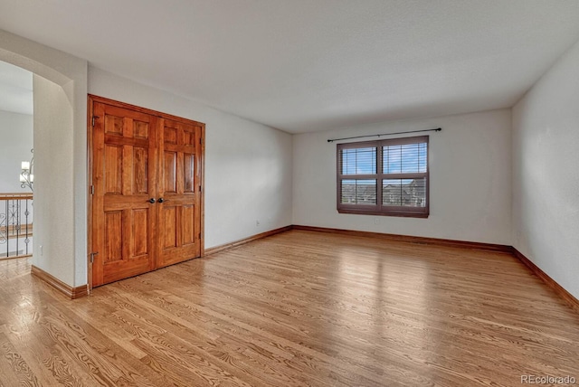 unfurnished room featuring an inviting chandelier, baseboards, light wood finished floors, and arched walkways