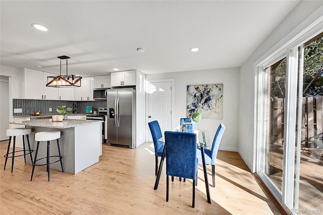 kitchen with tasteful backsplash, appliances with stainless steel finishes, white cabinetry, light wood-type flooring, and pendant lighting