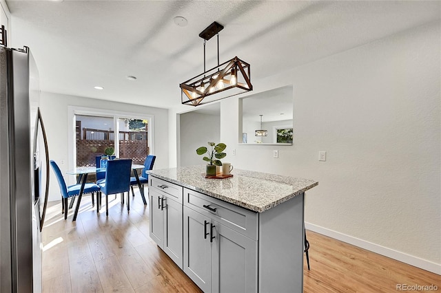 kitchen featuring a kitchen island, hanging light fixtures, stainless steel refrigerator with ice dispenser, light wood-type flooring, and light stone counters