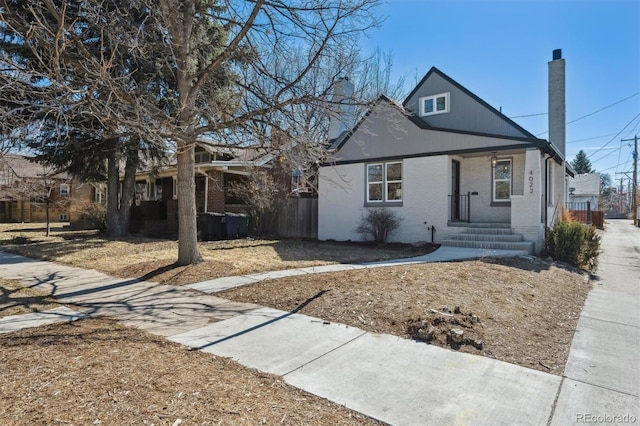 bungalow-style home with covered porch, a chimney, and brick siding